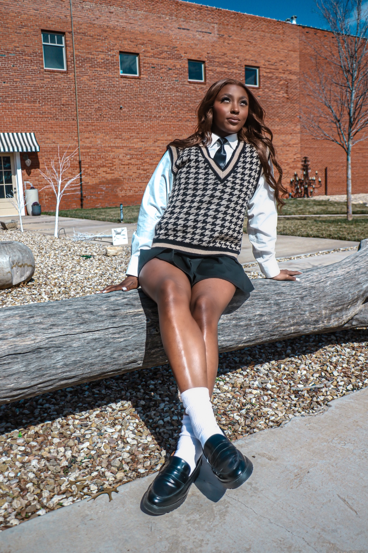 Senior-style portrait seated on a log against a brick wall