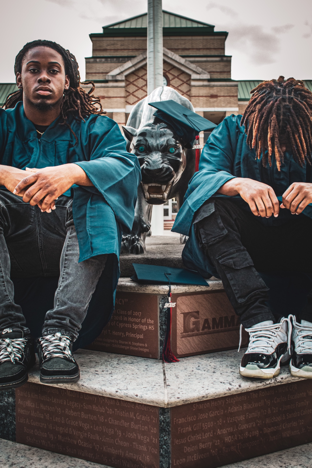 Graduation session — two graduates in caps and gowns at the campus panther statue